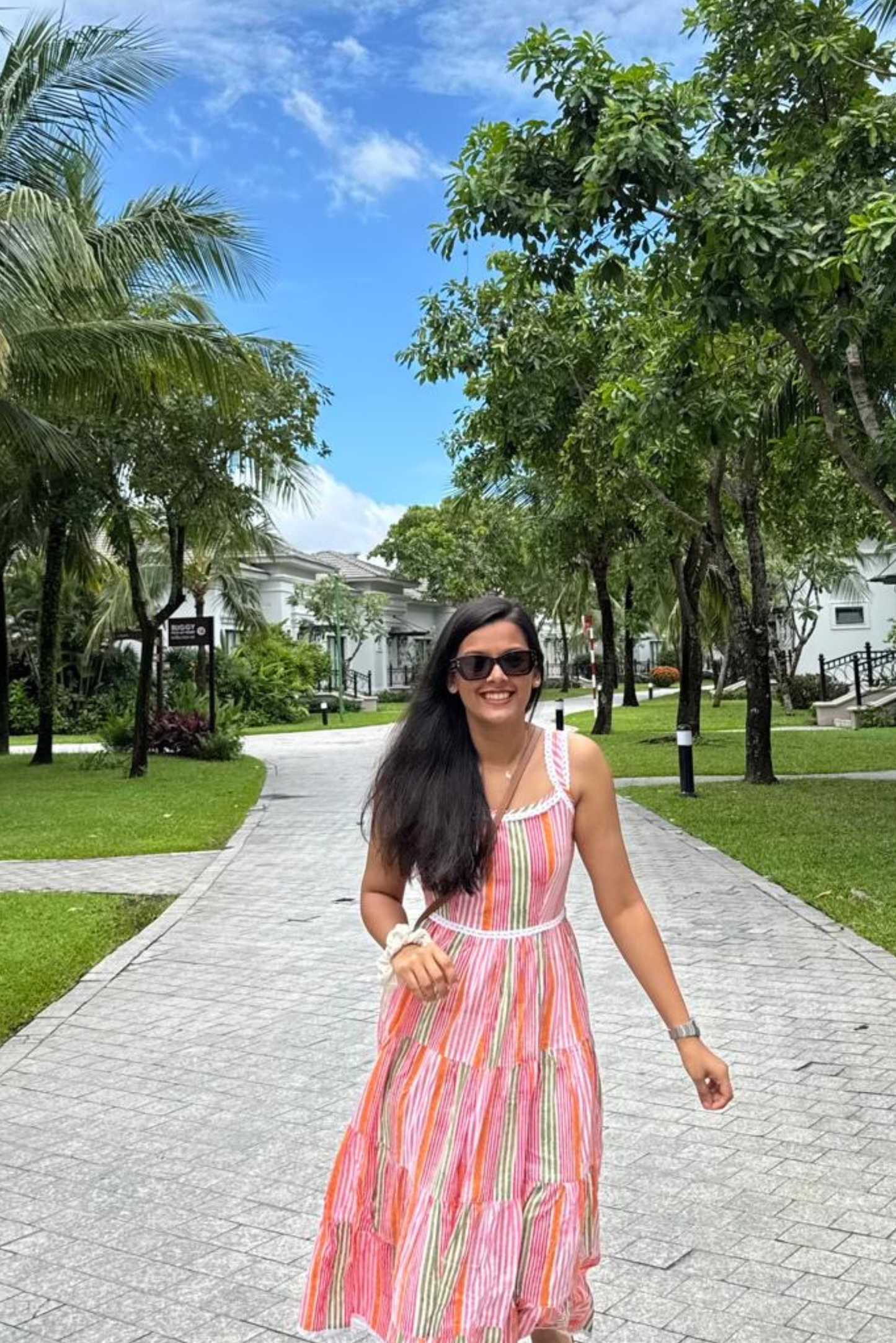 Woman in a colorful dress walking on a path with greenery and buildings in the background