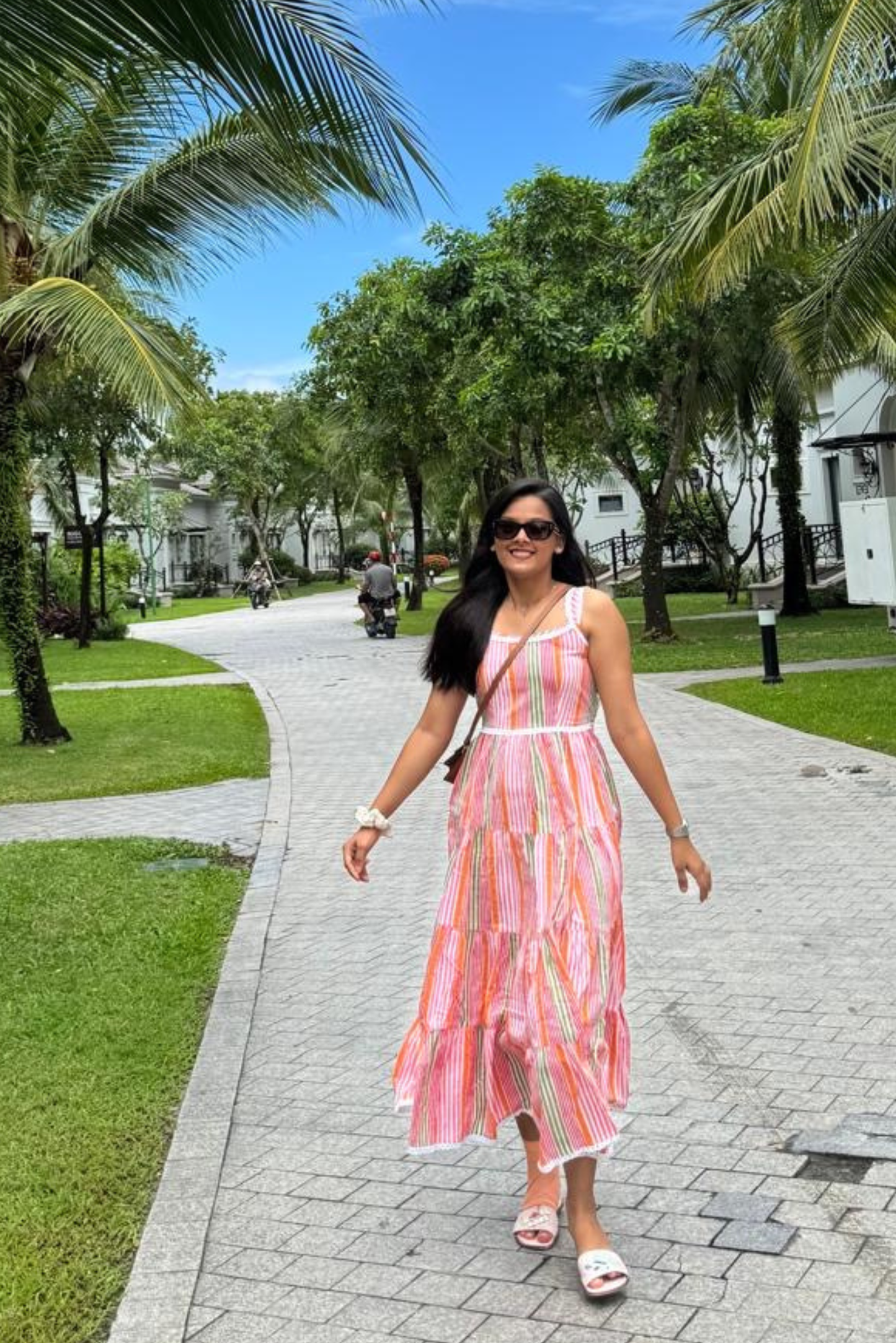 Woman in a striped dress walking on a sidewalk with palm trees in the background